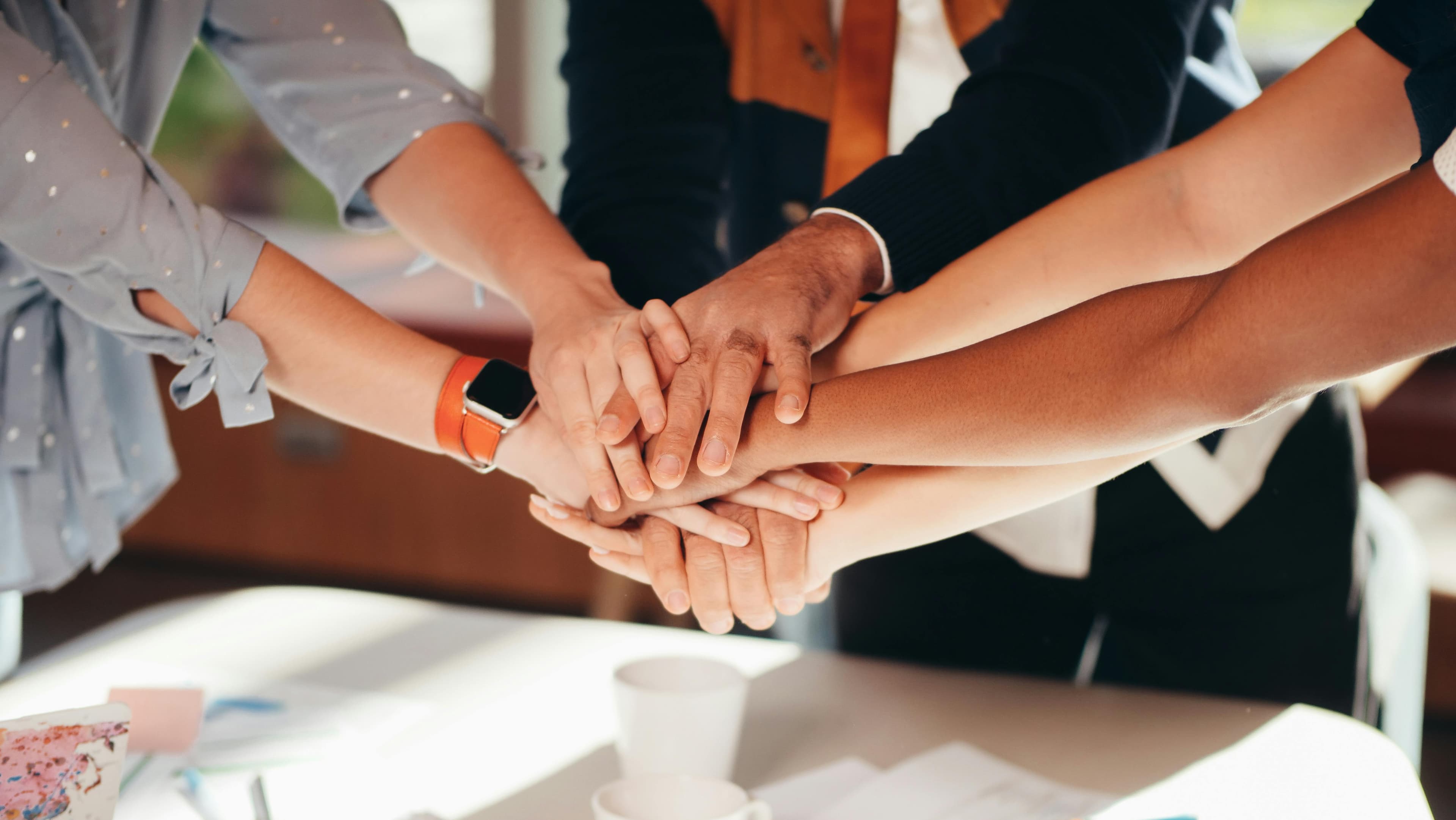 Un gruppo di persone sovrappone le mani in segno di collaborazione e spirito di squadra, attorno a un tavolo da lavoro.