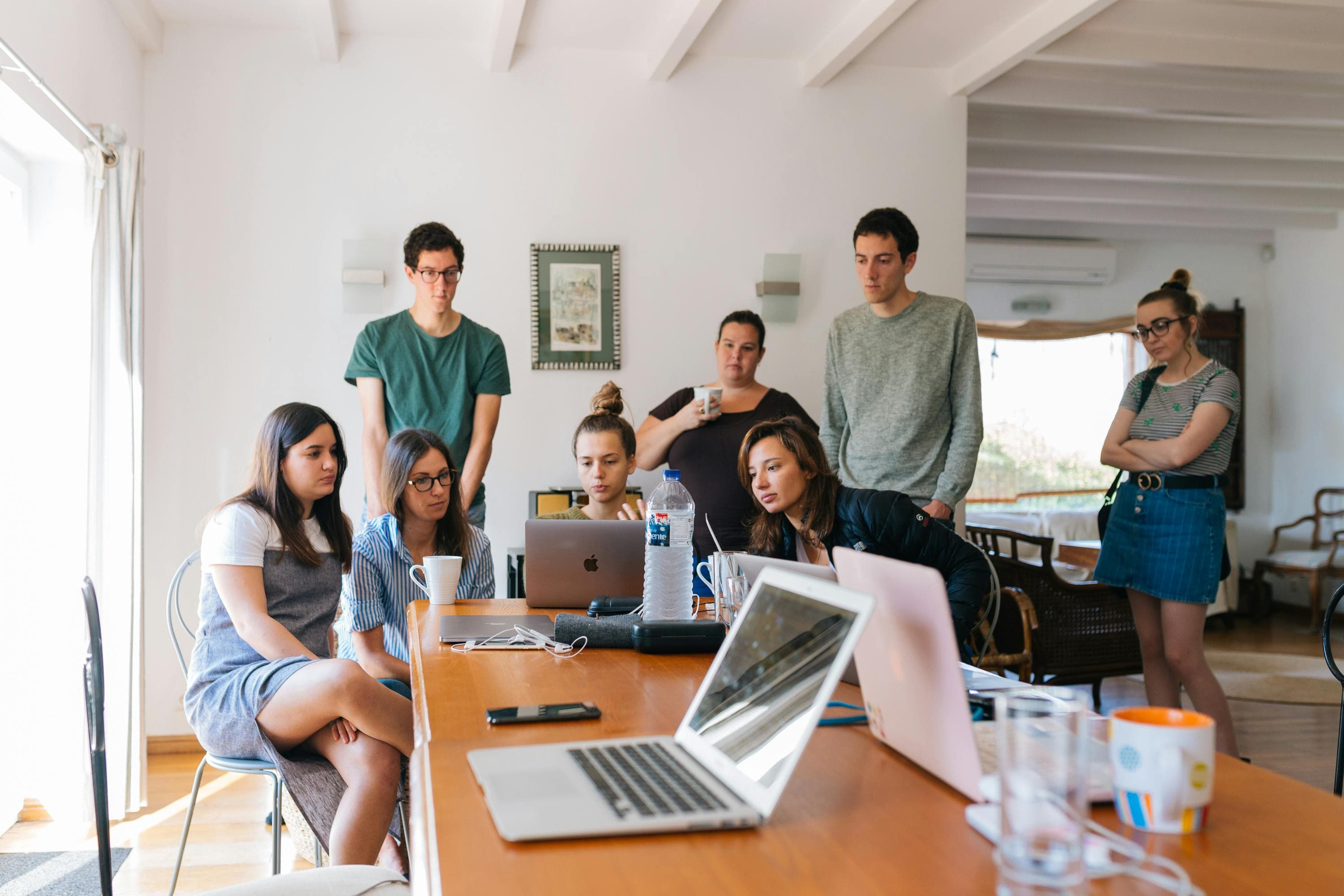 Un gruppo di giovani adulti è riunito attorno a un tavolo, concentrato su un laptop, in un ambiente informale e collaborativo.