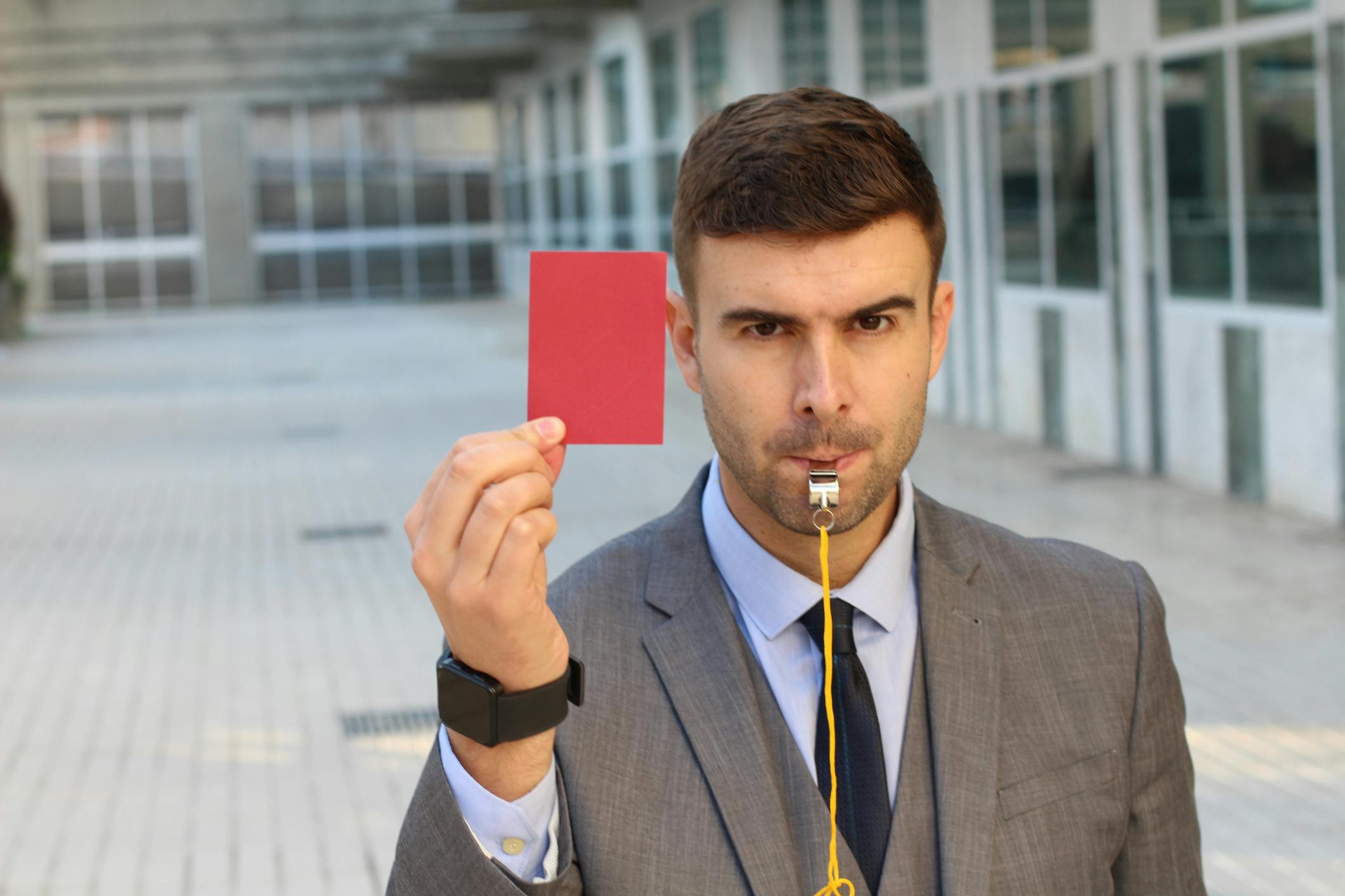 un uomo che usa il fischietto mentre tiene in mano un cartellino rosso 